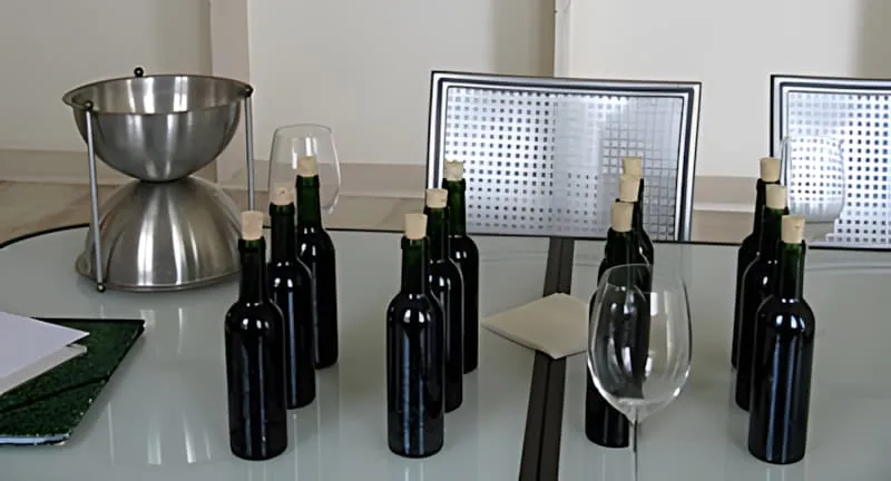 正式的品酒设置，桌上摆放着多瓶深色酒瓶、银色吐酒器和酒杯。