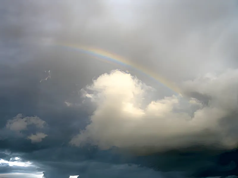 一道部分彩虹穿过乡村景观上的灰色暴雨云。
