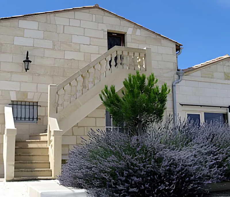 Des marches en pierre menant vers un bâtiment, bordées de plants de lavande violette en fleurs créant un passage parfumé.